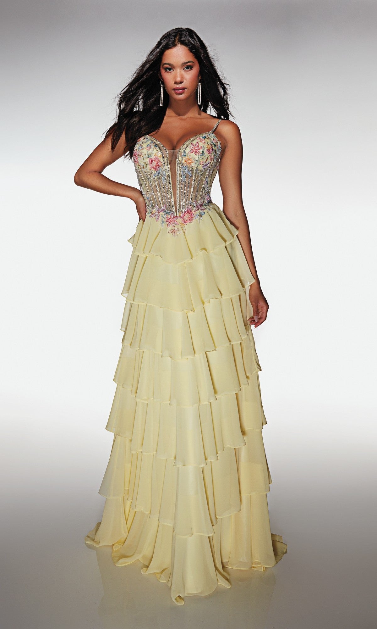 A woman poses against a plain background in the Alyce 61993 Long Prom Dress, a light yellow strapless gown featuring a chiffon tiered ruffle skirt and a fitted floral corset bodice.